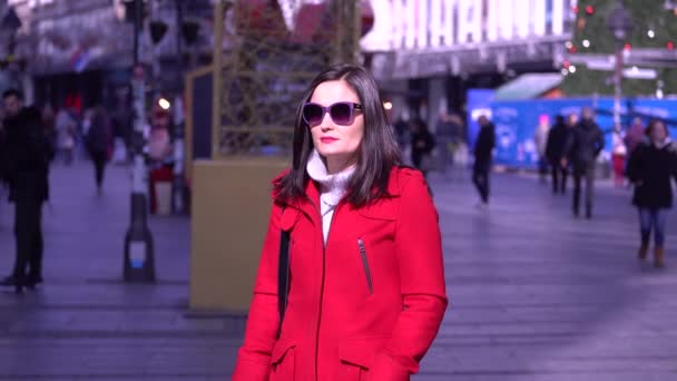 Μια γυναίκα με κόκκινο παλτό καπνίζει ένα τσιγάρο στη μέση μιας πλατείας. — Αρχείο Βίντεο