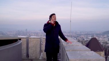 Kışın arka planda şehir manzarası olan bir adam dışarıda telefonla konuşuyor. 4K