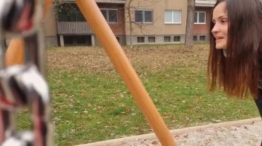 Kırmızı ceketli, mavi şapkalı, parkta salıncakta sallanan sevimli bir erkek bebek. Annesi onu öpüyor. Kış zamanı 4K yavaşlama