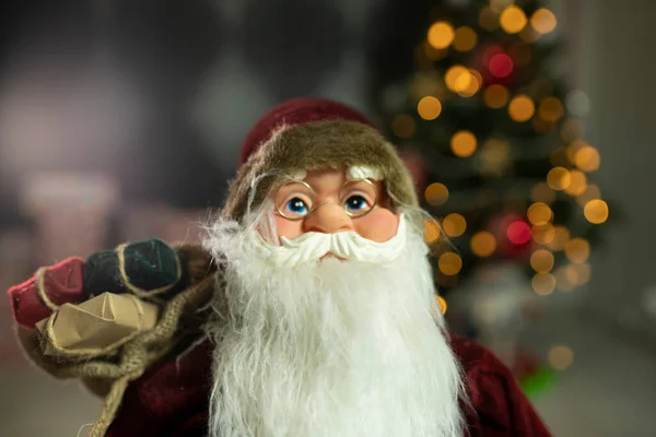 Noel Baba hediye dolu büyük bir çanta taşıyor, Noel ağacının yanında.