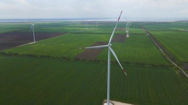 Geniş rüzgar türbinleri. Havadan bakıldığında mavi gökyüzü parkı yavaş çekim drone dönüşü. Yel değirmenlerinin siluetleri, yaz lensleri. alternatif enerji