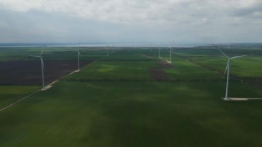 Geniş rüzgar türbinleri. Havadan bakıldığında mavi gökyüzü parkı yavaş çekim drone dönüşü. Yel değirmenlerinin siluetleri, yaz lensleri. alternatif enerji
