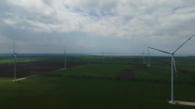 Geniş rüzgar türbinleri. Havadan bakıldığında mavi gökyüzü parkı yavaş çekim drone dönüşü. Yel değirmenlerinin siluetleri, yaz lensleri. alternatif enerji