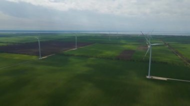 Geniş rüzgar türbinleri. Havadan bakıldığında mavi gökyüzü parkı yavaş çekim drone dönüşü. Yel değirmenlerinin siluetleri, yaz lensleri. alternatif enerji