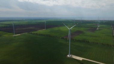 Geniş rüzgar türbinleri. Havadan bakıldığında mavi gökyüzü parkı yavaş çekim drone dönüşü. Yel değirmenlerinin siluetleri, yaz lensleri. alternatif enerji
