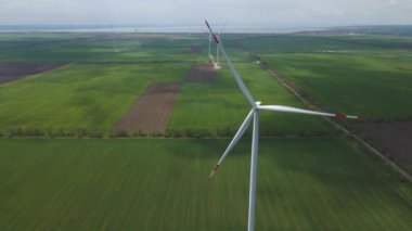 Geniş rüzgar türbinleri. Havadan bakıldığında mavi gökyüzü parkı yavaş çekim drone dönüşü. Yel değirmenlerinin siluetleri, yaz lensleri. alternatif enerji