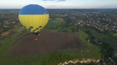 Renkli bir sıcak hava balonunun insansız hava aracı yeşil bir parkın üzerinde uçarken görüntüsü ve yazın gündoğumunda küçük bir Avrupa şehrinde bir nehir.