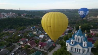 Renkli bir sıcak hava balonunun insansız hava aracı yeşil bir parkın üzerinde uçarken görüntüsü ve yazın gündoğumunda küçük bir Avrupa şehrinde bir nehir.