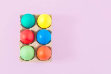 Açık mor arka planda yumurta kartonunda renkli paskalya yumurtaları. En az yaratıcı kopya alanı bileşimi.