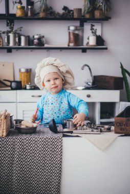 Aşçı şapkalı çocuk ve kepçe mutfakta.