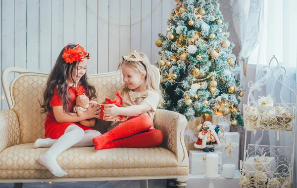 İki genç kız, süslenmiş bir Noel ağacının arka planında hediyelerini değiş tokuş ediyorlar.