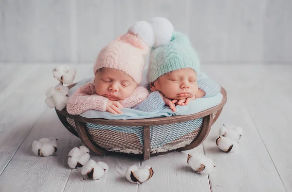 Twins are newborn brother and sister. Newborn girl and boy. Hats with white fur balls sleep sweetly in a basket.