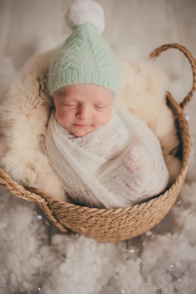 繭の位置の新生児が寝ていると彼の睡眠中に笑みを浮かべている 彼はミント色の帽子をかぶり 白い毛皮のバスケットに入れます — ストック写真