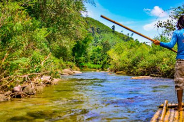 Ormanda rafting. Bambu salında sırıkla gezen siyah bir adam..
