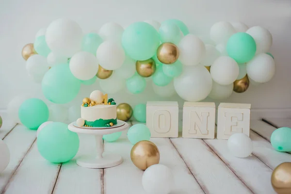 Stylish photo zone with mint, white and gold balls and a cake on a stand and one cubes.