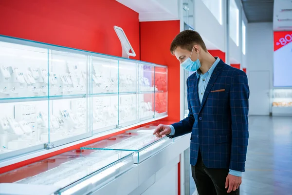 young man in a jewelry store in a jacket and a medical mask