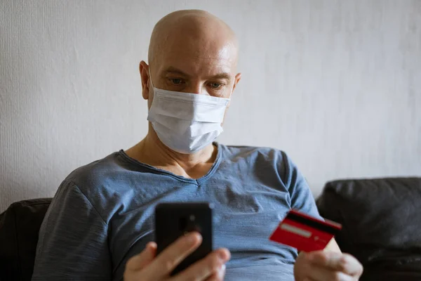 Bald man in protective mask with phone and credit card in hand