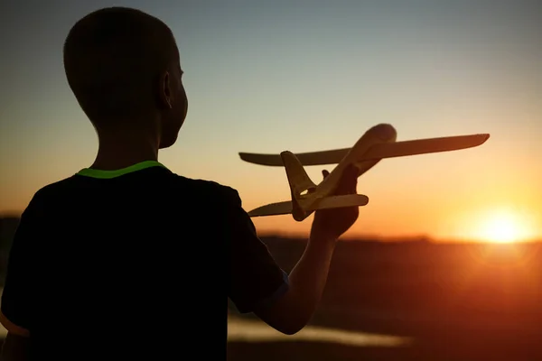 Boy throws a toy airplane in the summer at sunset.
