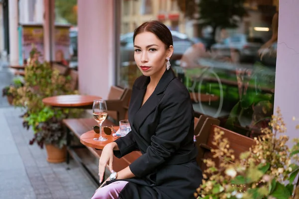 Beautiful woman sits in a street cafe with a glass of wine