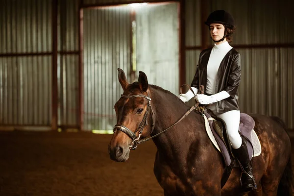 A jockey girl in full dress sits on a horse. Depicted: body fragment