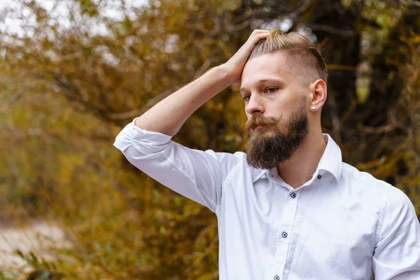 Autumn mood. Pensive young man in white shirt, meditates and walks in park