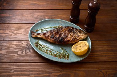 Akdeniz mutfağı kavramları için ideal ahşap masa üzerinde limon ve bitki sosuyla servis edilen rostoskopik ızgara balık..