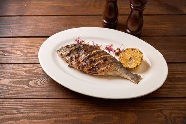 Kömürleşmiş limon ve ahşap tabakta mikro yeşillikle servis edilen ızgara balık, zarif bir restoran deniz ürünleri sunumu..