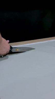 Mobilya üretimi sırasında atölye masasında büyük bir terzi makasıyla açık gri döşeme malzemesi kesmeye dikey yakın çekim.