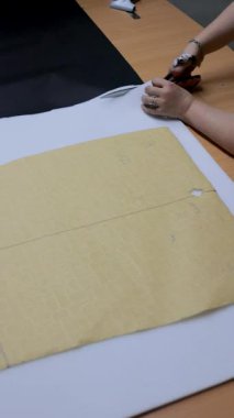 Mobilya üretim sürecinde atölye masasında kağıt şablonu takip eden makas ile döşeme köpüğü kesen zanaatkârın dikey görünümü.