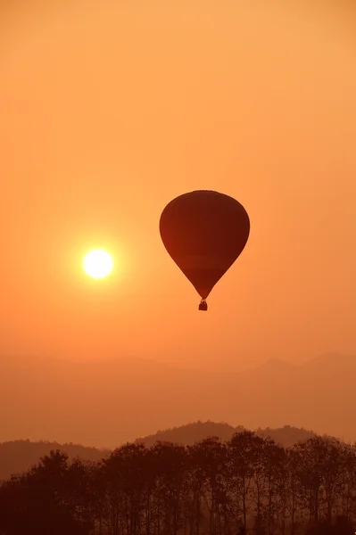 Balão de ar quente colorido está voando ao pôr do sol — Fotografia de Stock