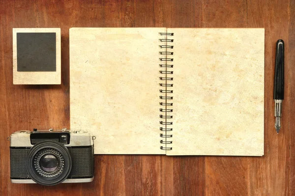 Tom anteckningsbok med penna, fotoramar och kamera på trä bakgrund — Stockfoto