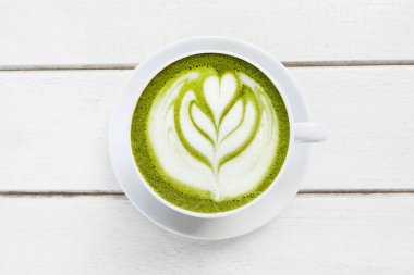Bir fincan yeşil çay, ahşap beyaz arka planda matcha latte.                                                                                    