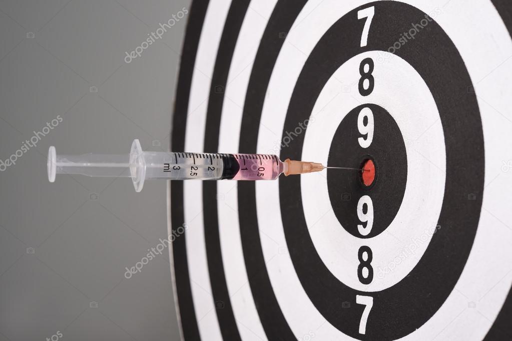 Syringe in dart board on gray background