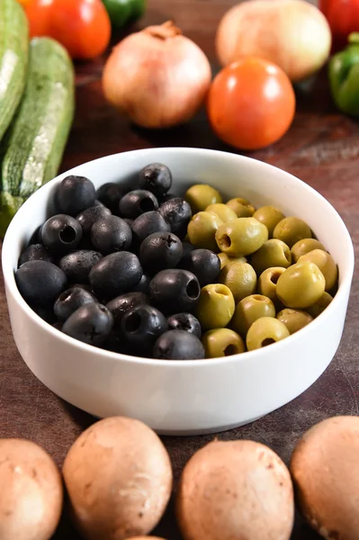 Olives vertes et noires dans un bol blanc et ingrédients pour pizza — Photo