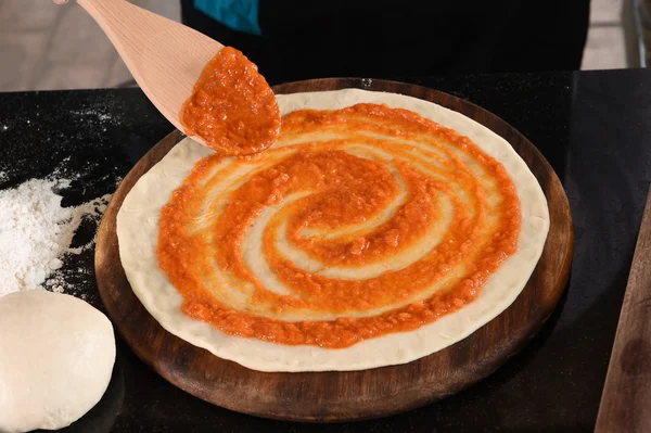 Dodając sos pomidorowy do pizzy podstawy — Zdjęcie stockowe