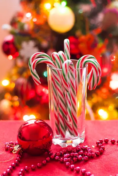 Sweet canes in the glass on the background of the Christmas tree — Stock Photo, Image