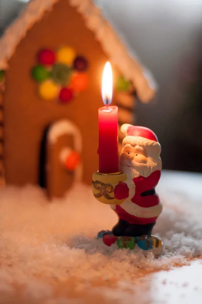Фигура Санта-Клауса на фоне пряничного домика, в котором горит свеча — стоковое фото