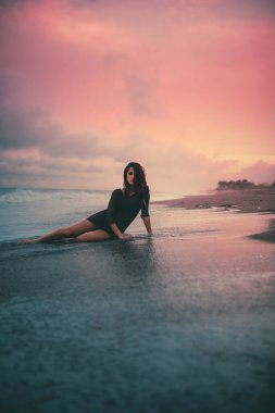 Okyanusun karşısındaki sahilde poz veren genç bir kadın.