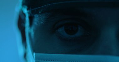 Düşük ışık, göz ve tıbbi maske takmış bir adamın görüntüsü.