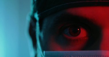 Kırmızı ışık, göz ve tıbbi maske takmış bir adamın kesilen görüntüsü.