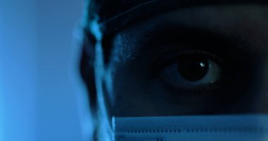 Düşük ışık, göz ve tıbbi maske takmış bir adamın görüntüsü.