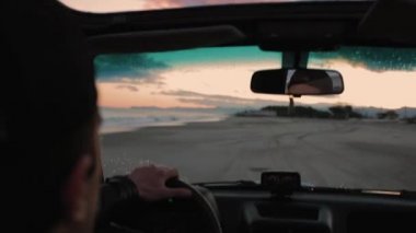 Gün batımında plajda araba süren genç bir adam. 