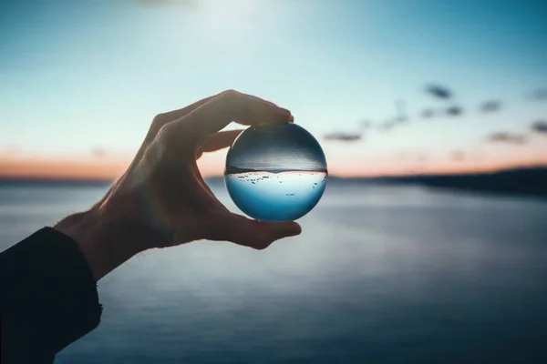 Mano Sosteniendo Bola Cristal Durante Amanecer Sobre Paisaje Marino —  Fotos de Stock