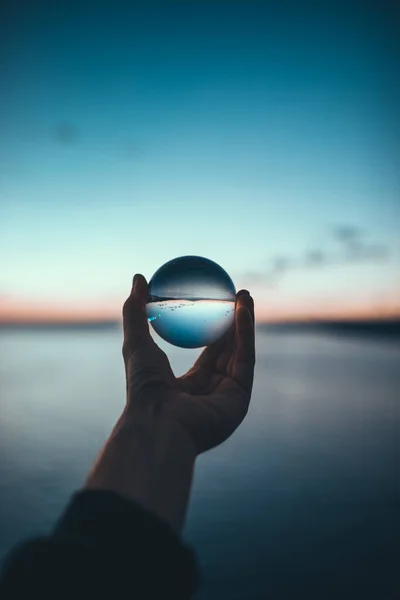 Mano Sosteniendo Bola Cristal Durante Amanecer Sobre Paisaje Marino —  Fotos de Stock