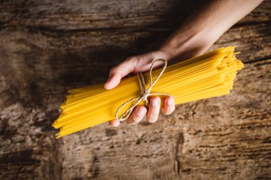 Ahşap masada sarı, uzun bir spagetti tutan el. Çiğ spagetti..