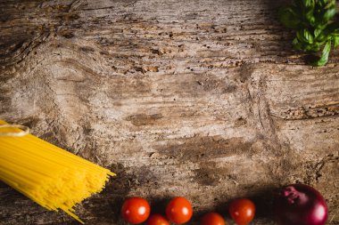 Tahta bir masada kiraz domatesli ve soğanlı sarı uzun spagetti. Sarı İtalyan makarnası. Çiğ spagetti..