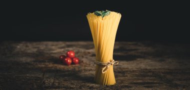 Tahta masadaki kiraz domatesli sarı uzun spagetti. Sarı İtalyan makarnası. Çiğ spagetti..