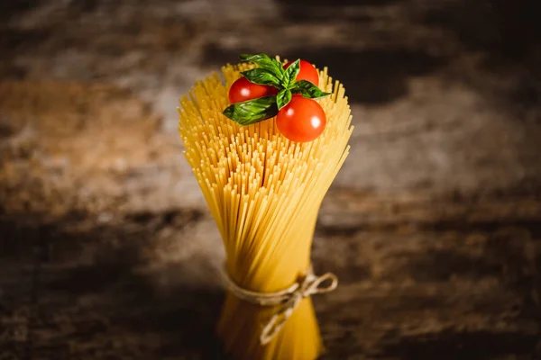 Tahta masadaki kiraz domatesli sarı uzun spagetti. Sarı İtalyan makarnası. Çiğ spagetti..