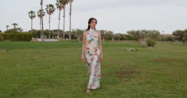 Uzun yaz elbiseli, çiçekli bir kadın yaz parkında yürüyor. 