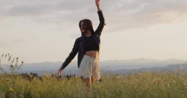 Beyaz şortlu, siyah deri ceketli gün batımında yaz tarlasında yürüyen genç bir kız.